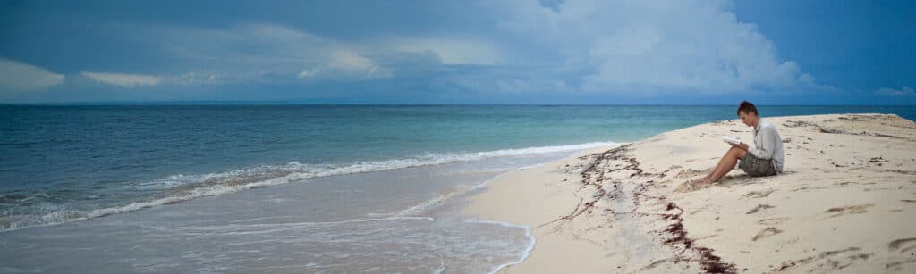 boy sitting on beach writing in journal