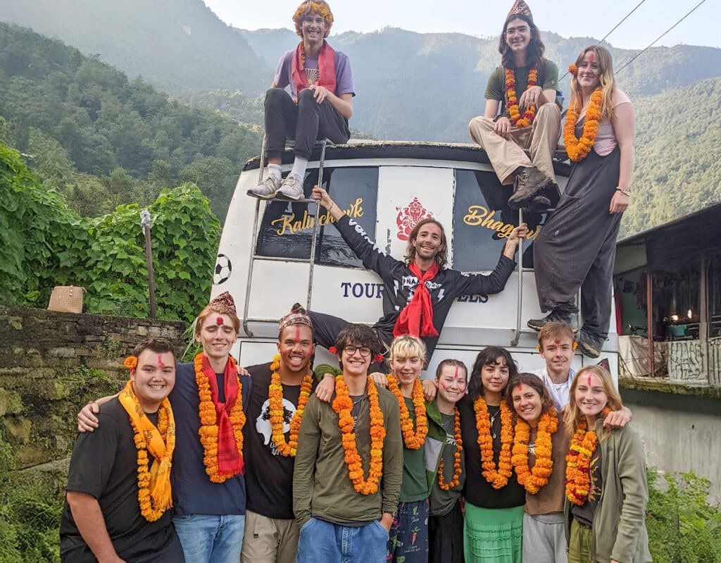 group smiling in front of van wearing marigold necklaces