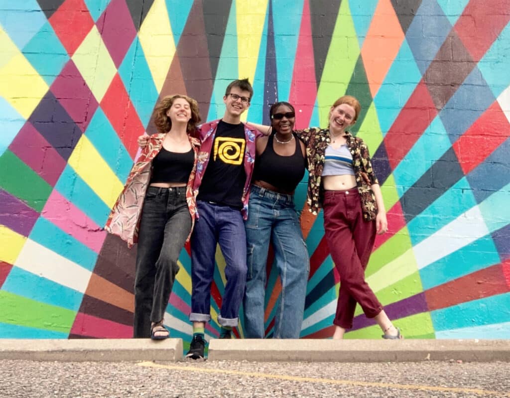 group of four posing before colorful mural